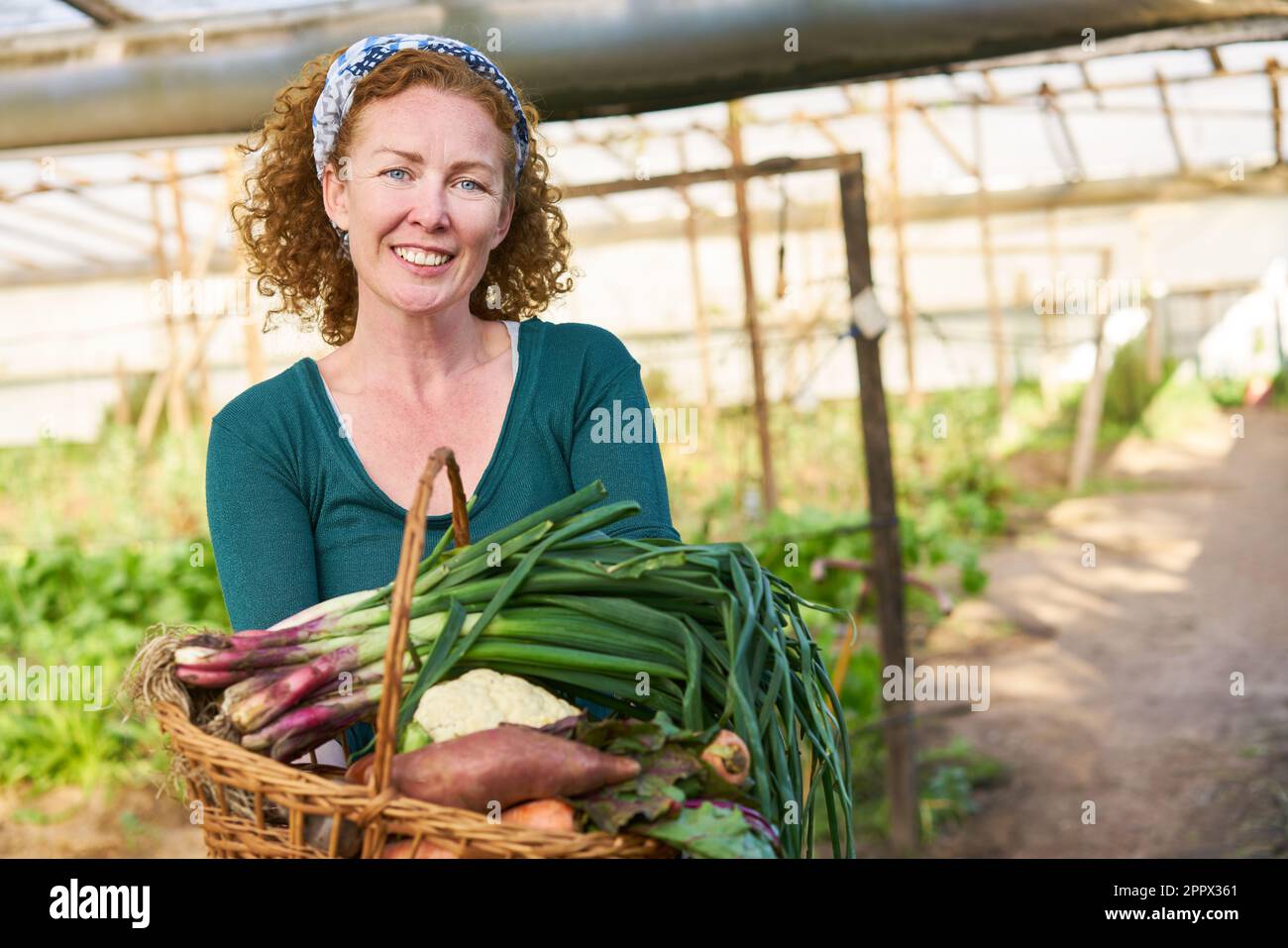 Portrait of smiling mature female farmer holding fresh vegetables ...