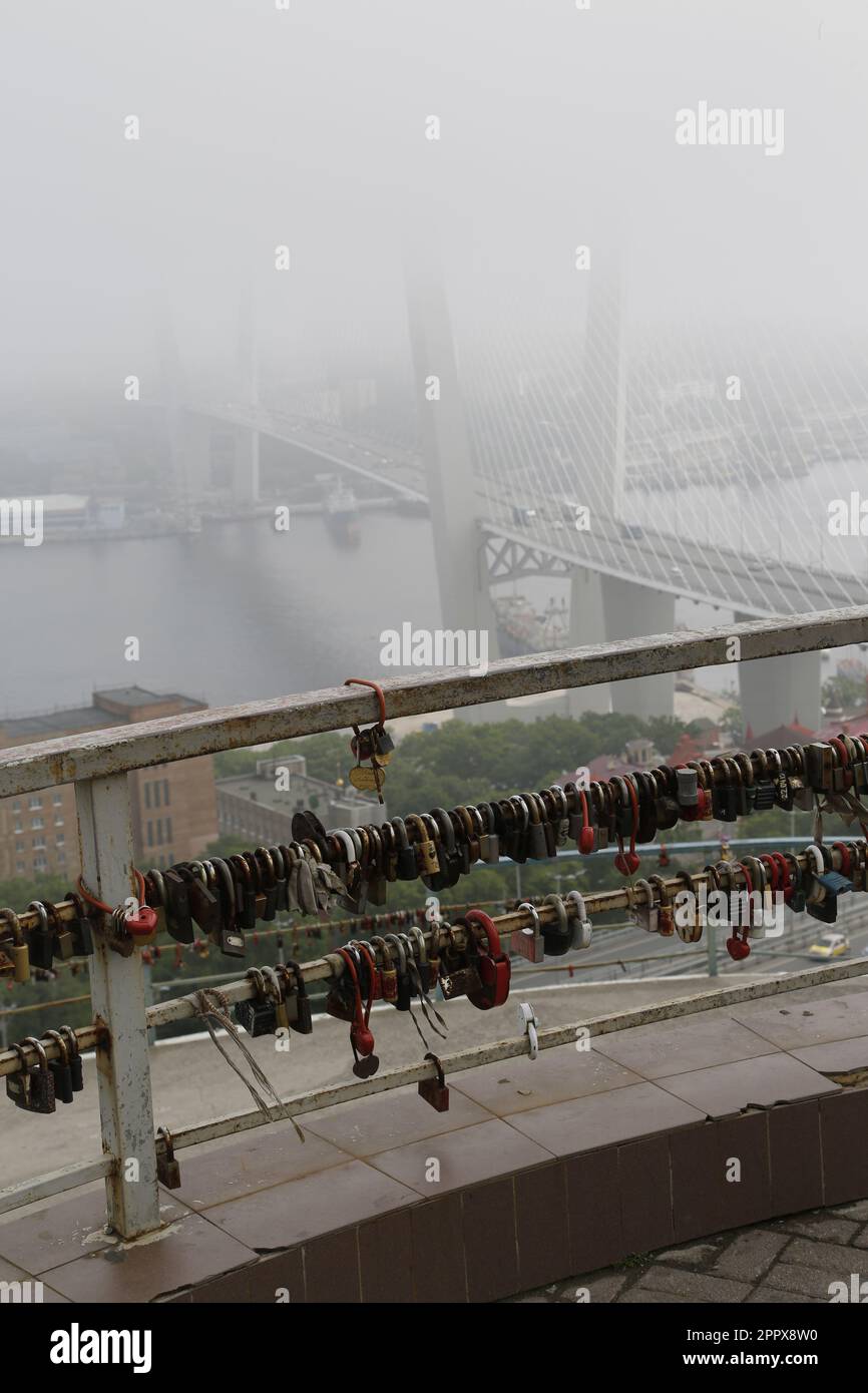 Love locks (love padlocks) on Eagle's Nest hill (Orlinoye Gnezdo Hill) in Vladivostok, Russia,,with view on Golden Bridge (Золотой мост, Zolotoy Most) Stock Photo