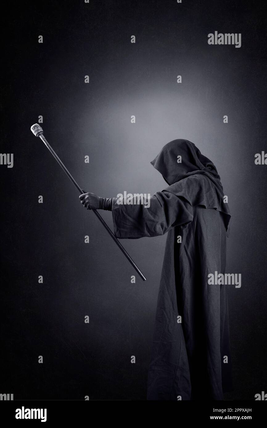 Wizard with hooded cape and magic staff over dark misty background Stock Photo