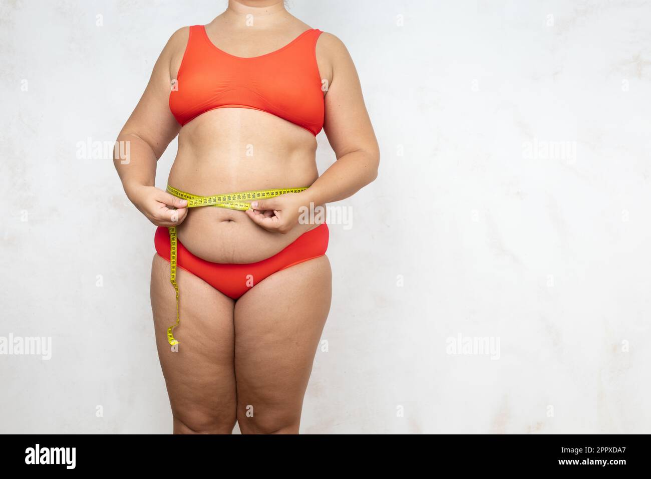 Overweight woman measure waist circumference with tape, white