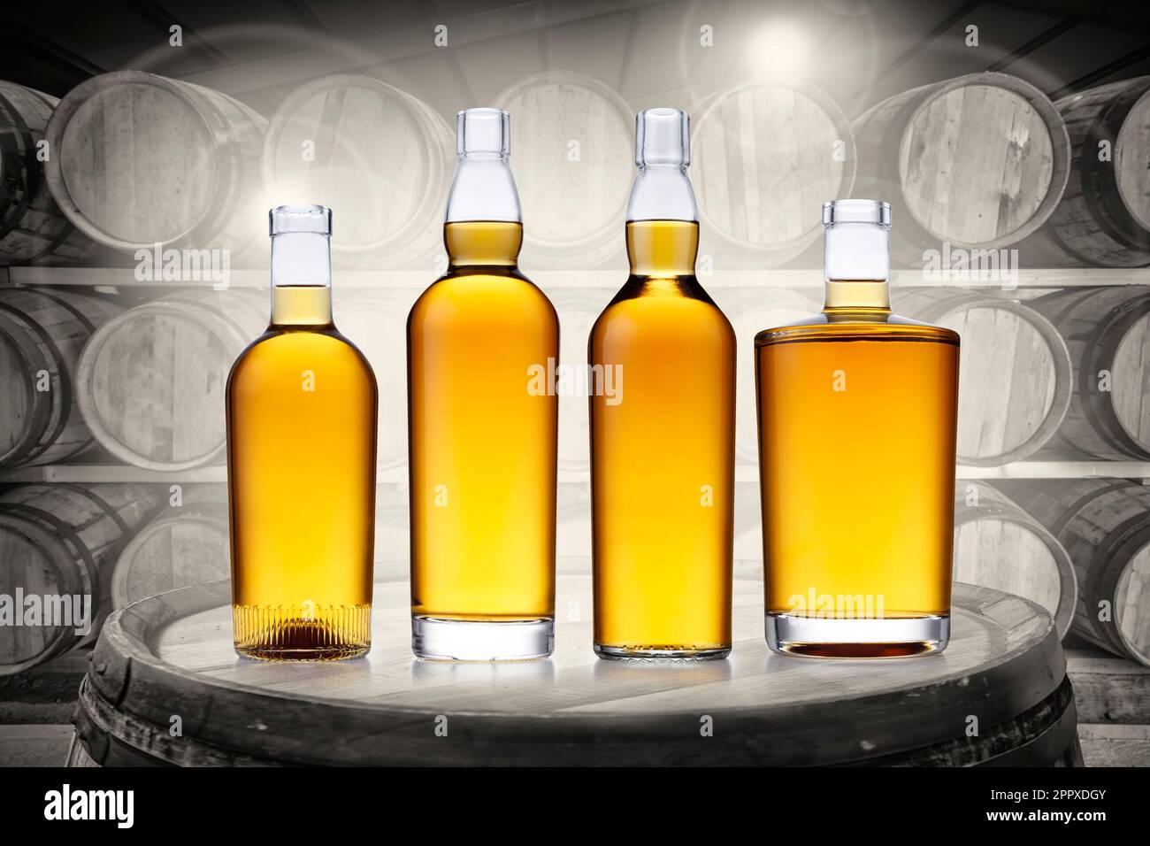 4 bottles of glowing amber whisky, set on top of an old barrel, in a black and white barrel
