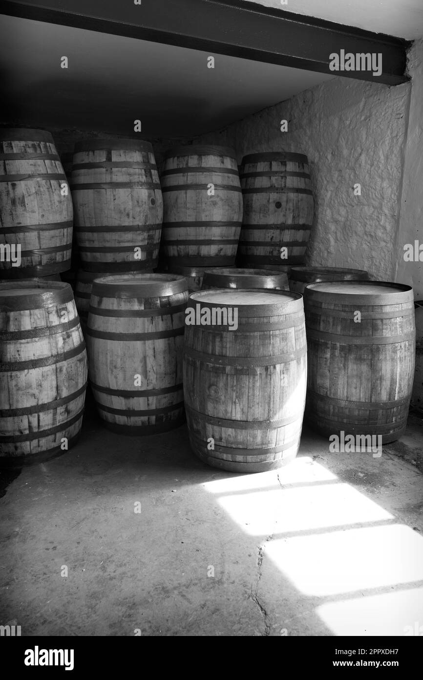 Black and white old whisky barrels, stacked in a warehouse ready to fill with raw spirit and leave to mature over time, in a dusty warehouse with ligh Stock Photo