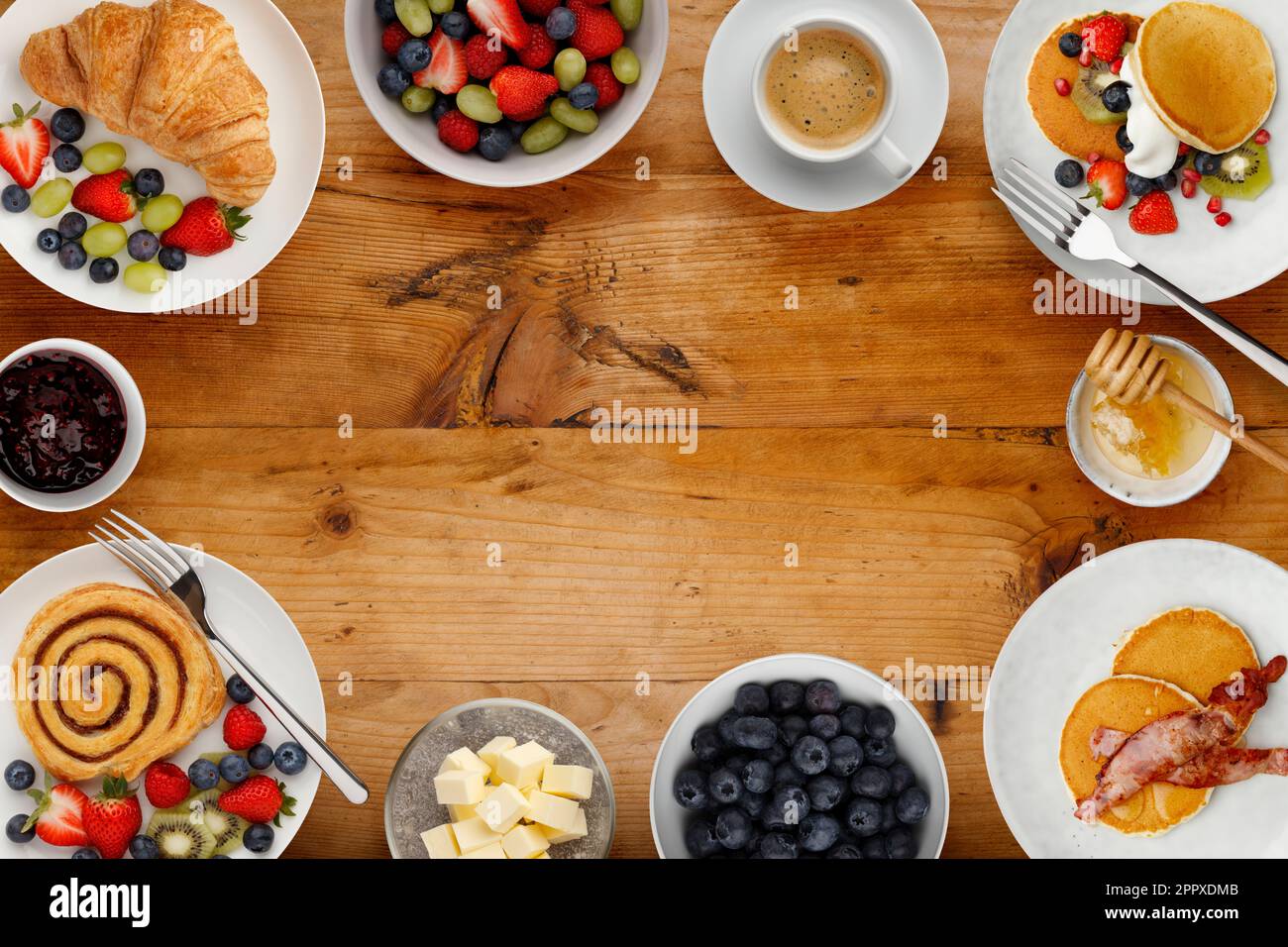 A border of delicious breakfast plates, pancakes and pasteries, bowls of fruit and porridge, and cups of coffee, on a rustic wooden background Stock Photo