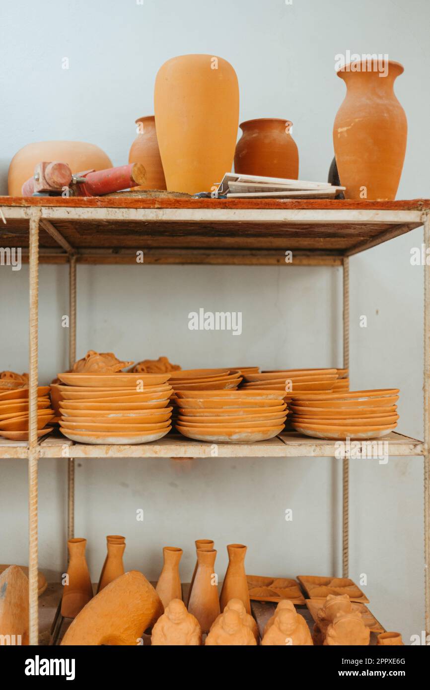 Collection of various handmade clay vases and different plates arranged on shelves against white background in workshop Stock Photo