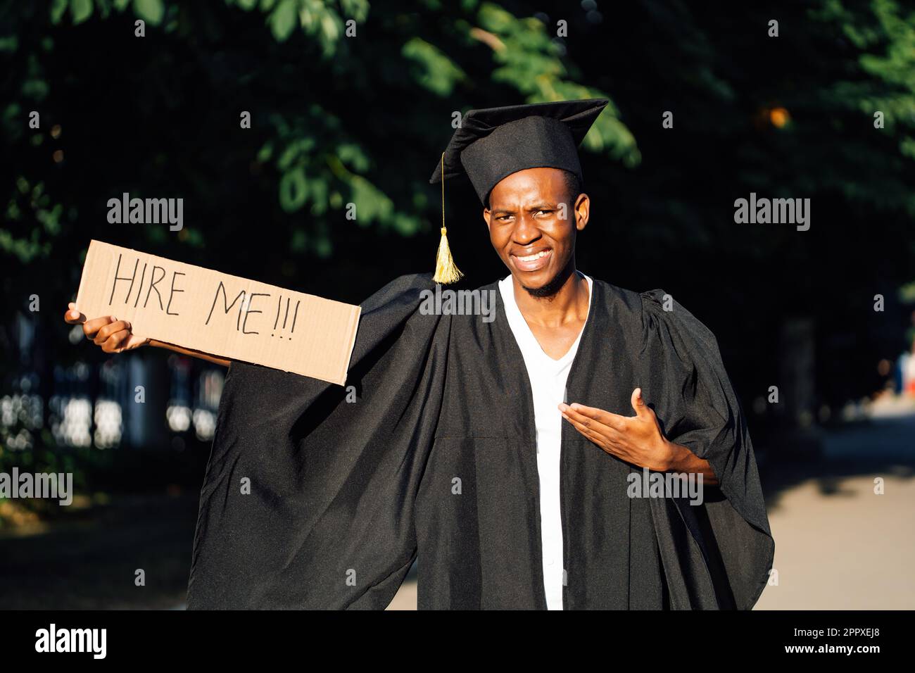 Portrait of smiling black guy standing and pointing at cardboard poster on street in sunny day looking for job, employment issue. University or Stock Photo