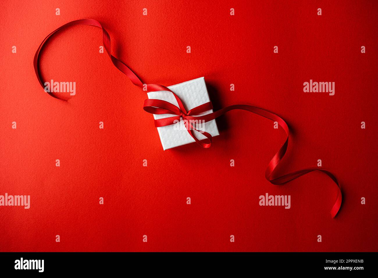 White gift box with red ribbon on bright red background Stock Photo