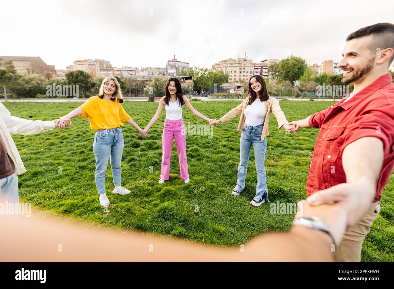 Young group of diverse friends in circle holding hands in a park Stock