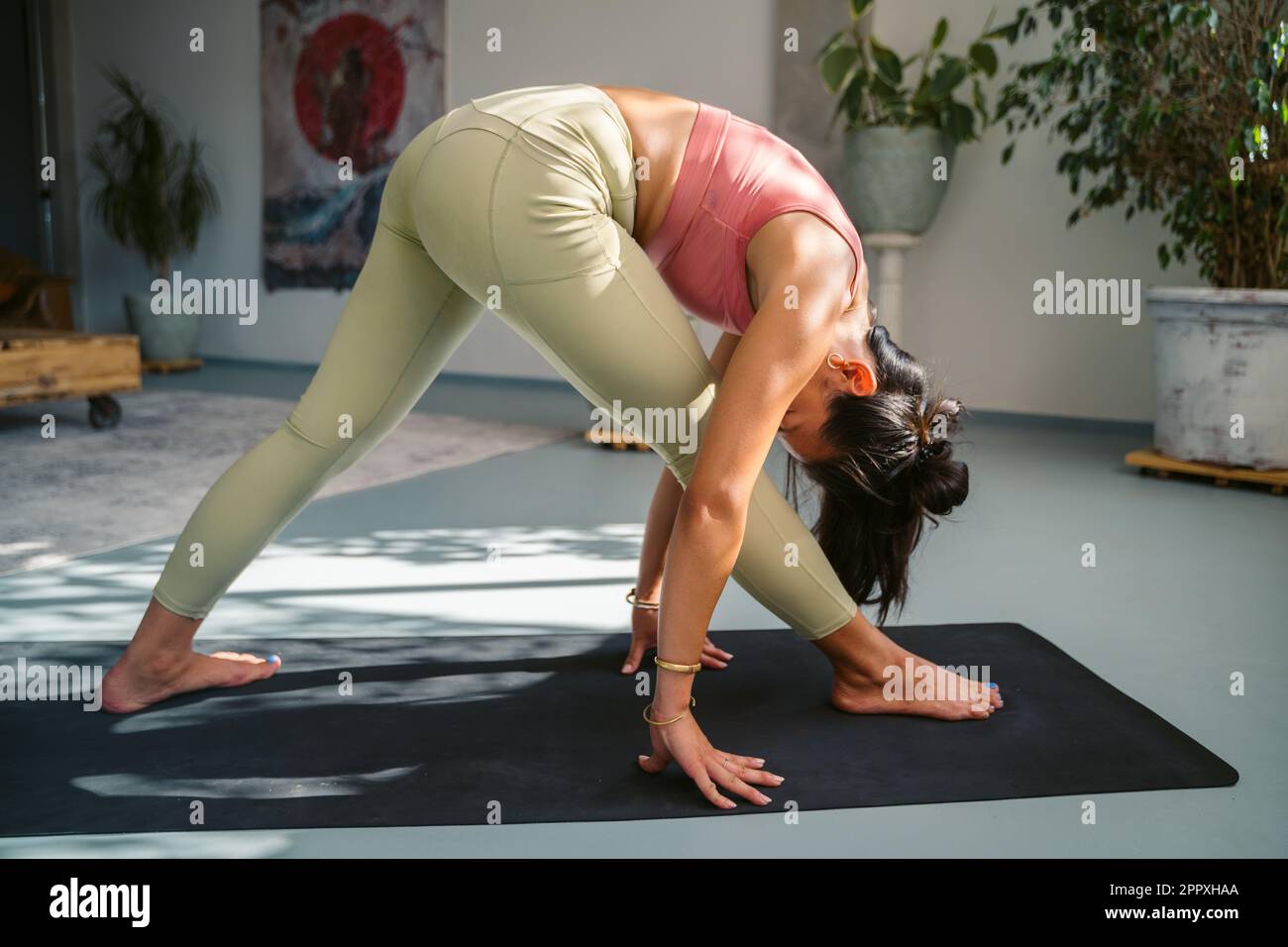Full body side view of slim young barefoot female in activewear performing Pyramid with Arms Extended pose while practicing yoga on mat in modern stud Stock Photo