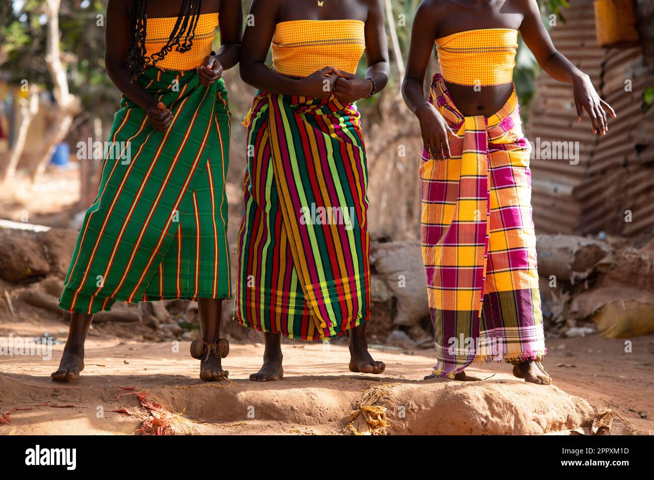 Cropped unrecognizable African girls in traditional clothes dancing on dusty road near green trees in Guinea-Bissau Stock Photo