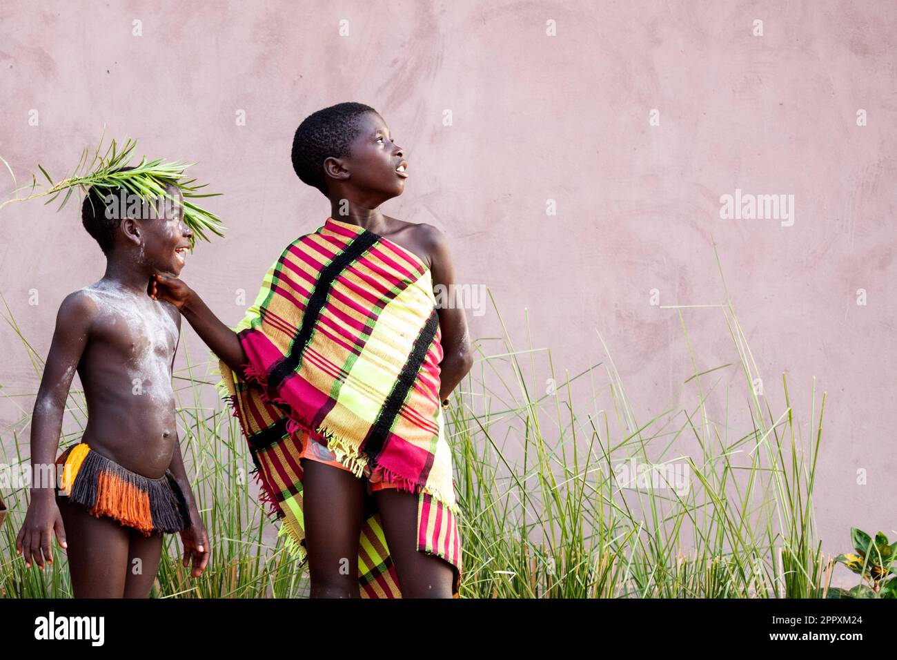 Full body of African tribal boys in traditional outfits standing in row near building wall and looking away in Guinea Bissau Stock Photo