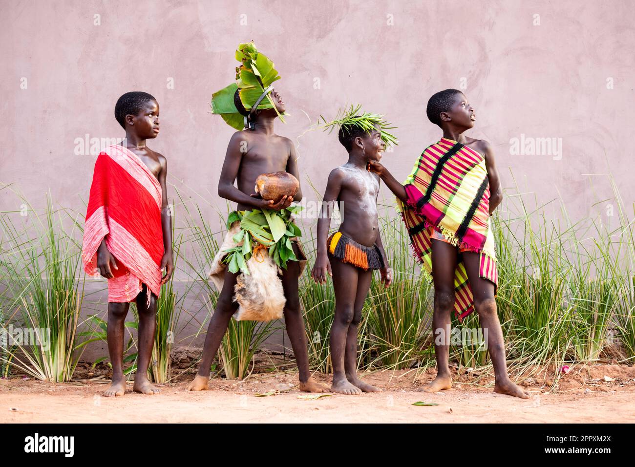 Full body of African tribal boys in traditional outfits standing in row near building wall and looking away in Guinea Bissau Stock Photo