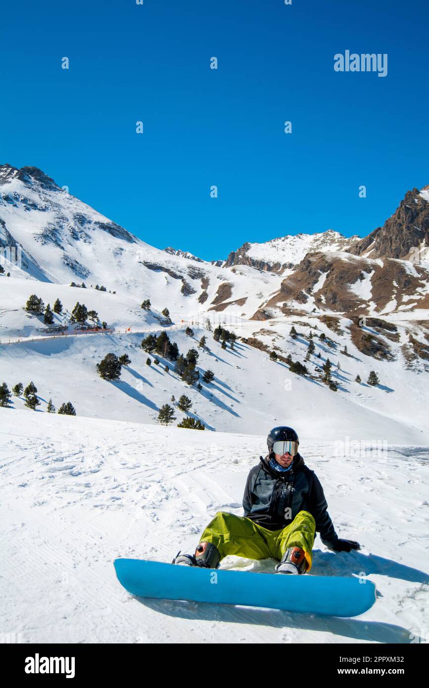 Full body of anonymous snowboarder in ski suit and with snowboard resting on snowy ground while spending winter vacation Stock Photo