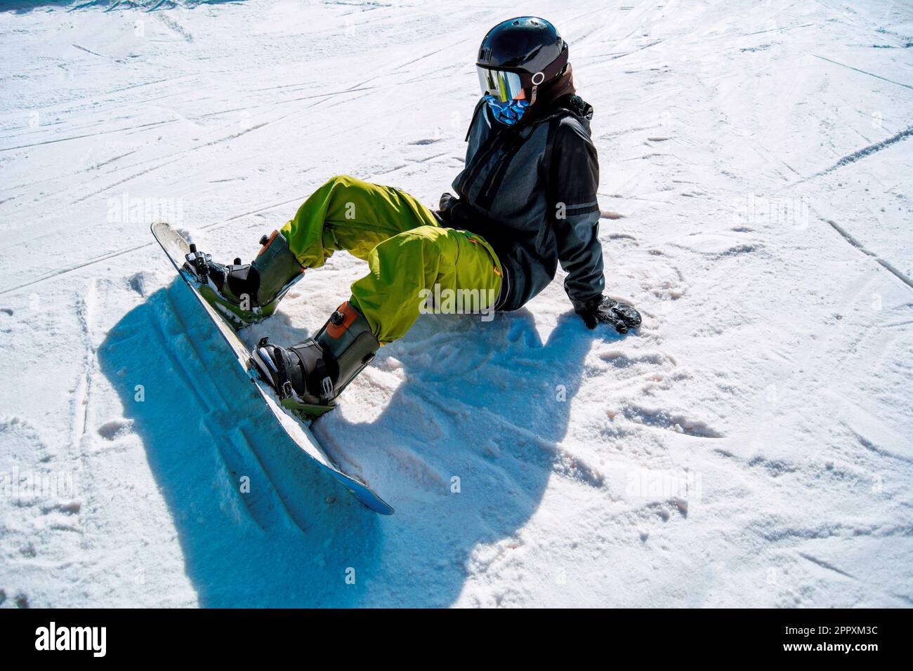 Full body of anonymous snowboarder in ski suit and with snowboard resting on snowy ground while spending winter vacation Stock Photo