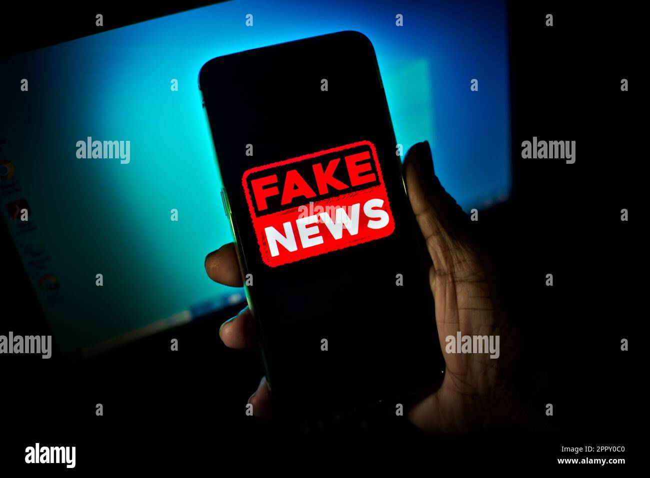 Hand holding a cell phone where the words fake news are shown on the screen. low-light, dramatic image suggesting danger or a dangerous attitude. Stock Photo