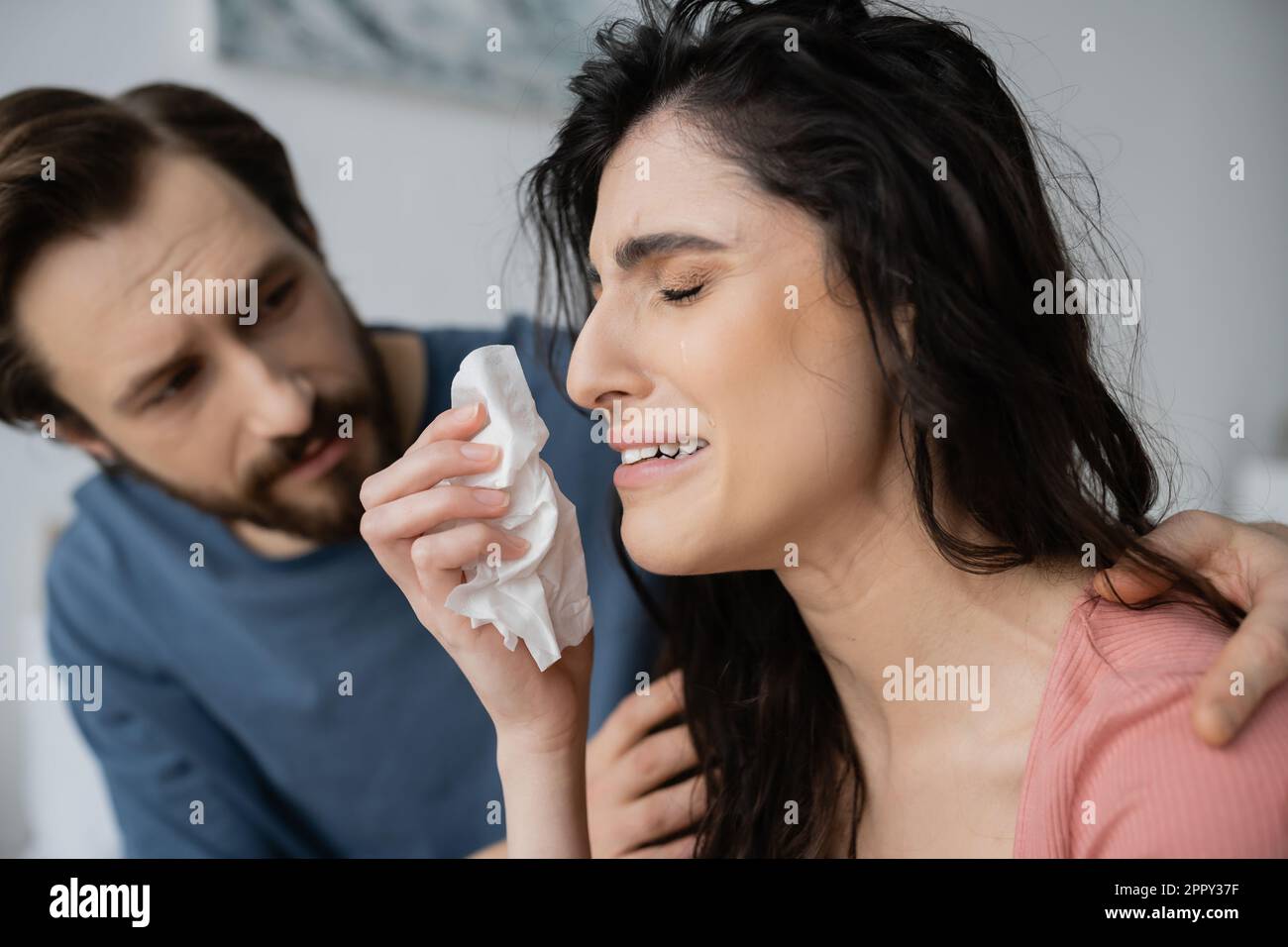 Blurred man calming down displeased and crying girlfriend with napkin at home,stock image Stock Photo