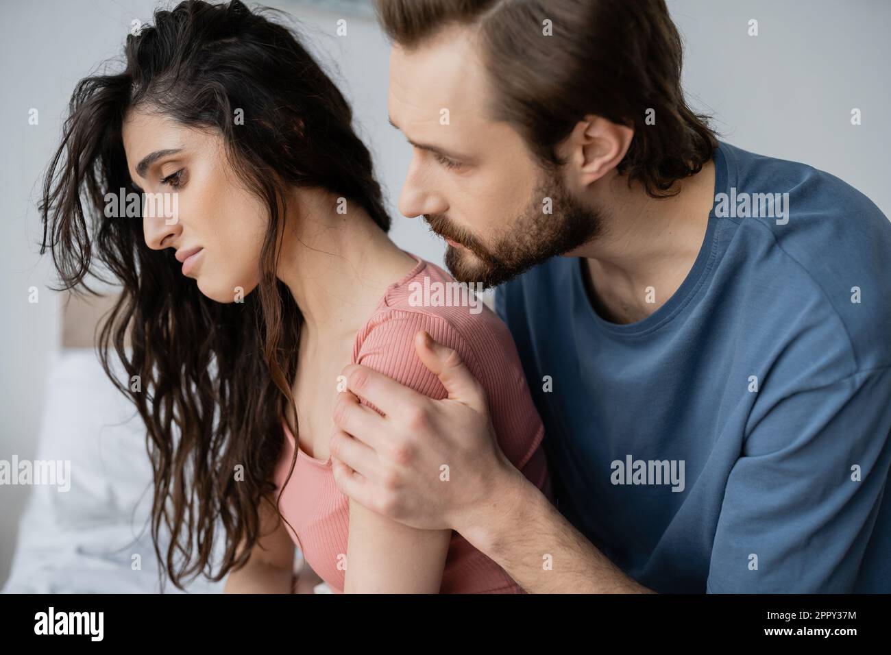 Caring bearded man calming down displeased girlfriend in bedroom at home,stock image Stock Photo