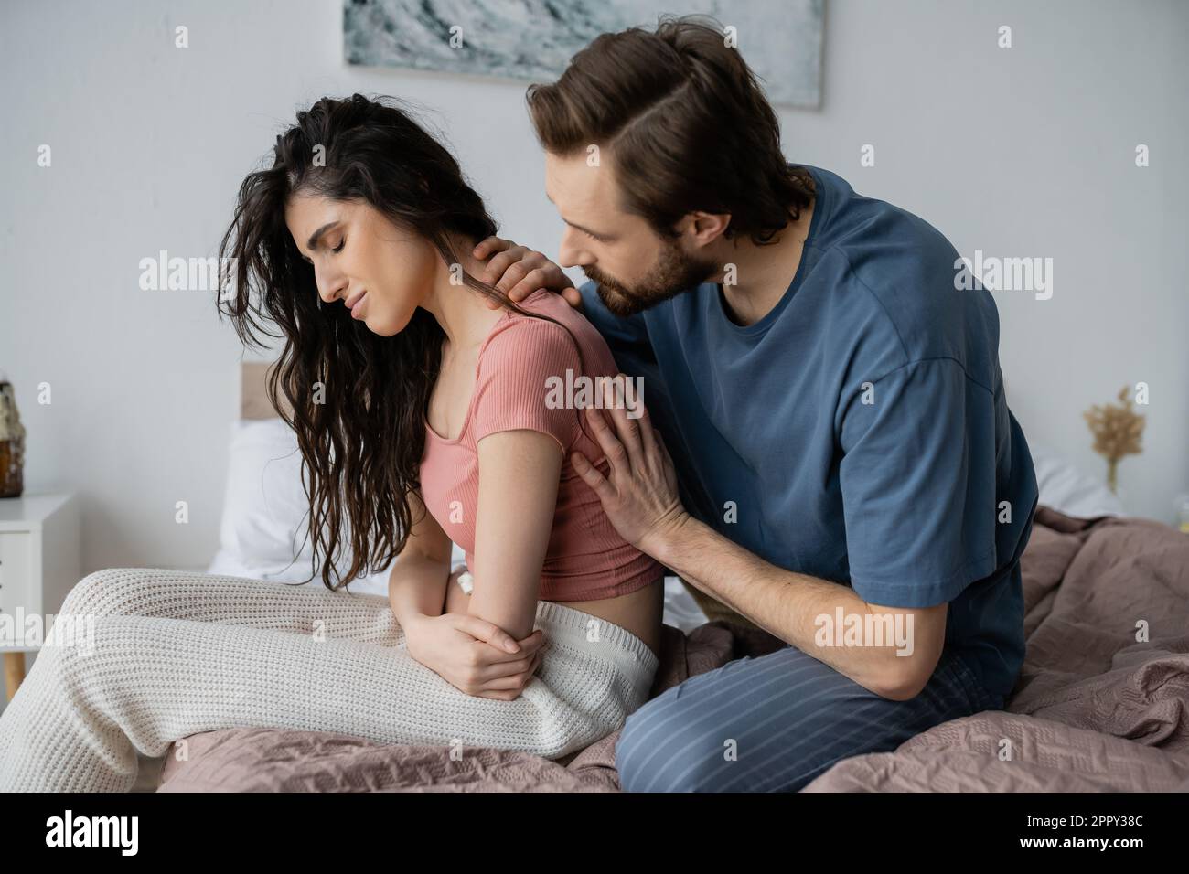 Bearded man calming disappointed girlfriend in pajama in bedroom,stock image Stock Photo