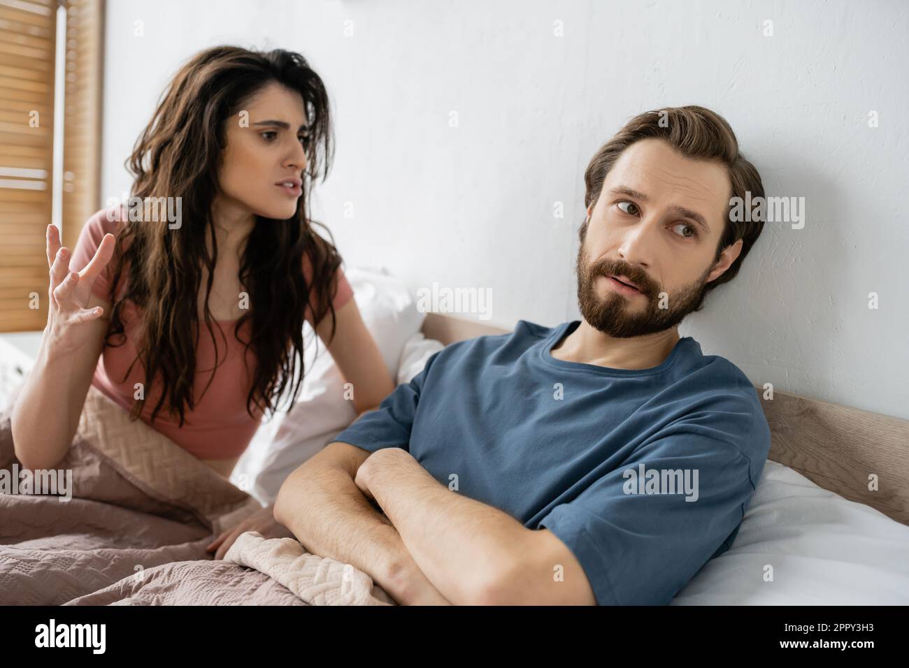 Angry woman talking to bearded boyfriend crossing arms on bed at home,stock image Stock Photo