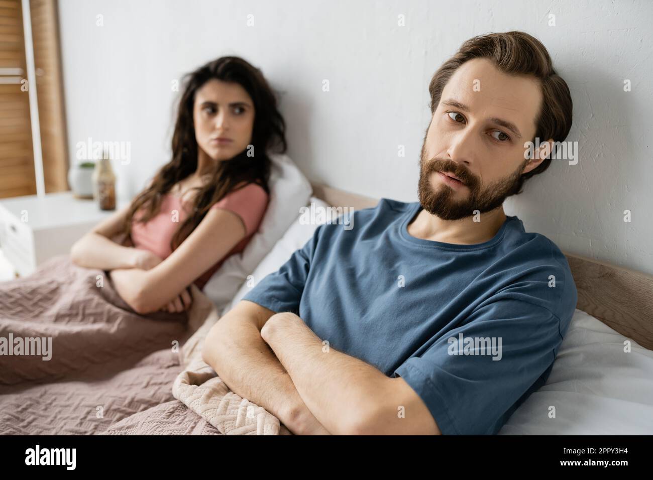 Nervous man crossing arms while sitting near blurred girlfriend on bed at home,stock image Stock Photo