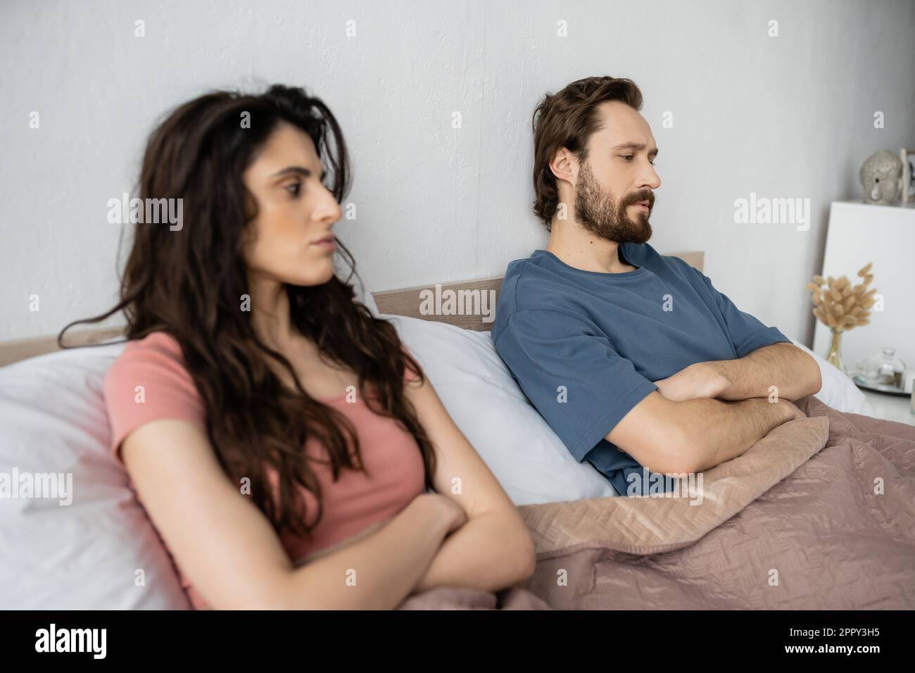 Dissatisfied man crossing arms while sitting near blurred girlfriend on bed at home,stock image Stock Photo