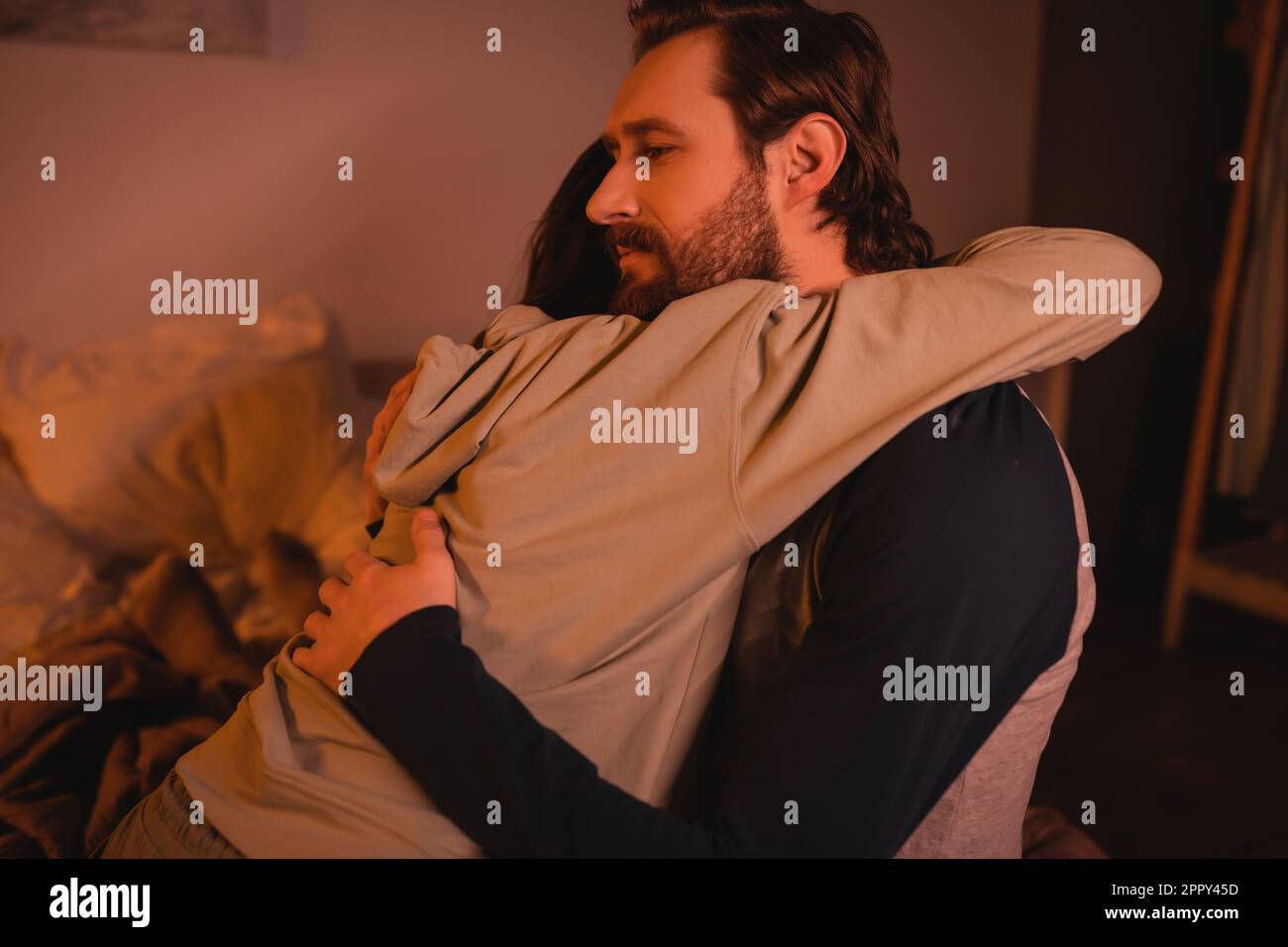 Bearded man hugging and calming down girlfriend in bedroom at night,stock image Stock Photo