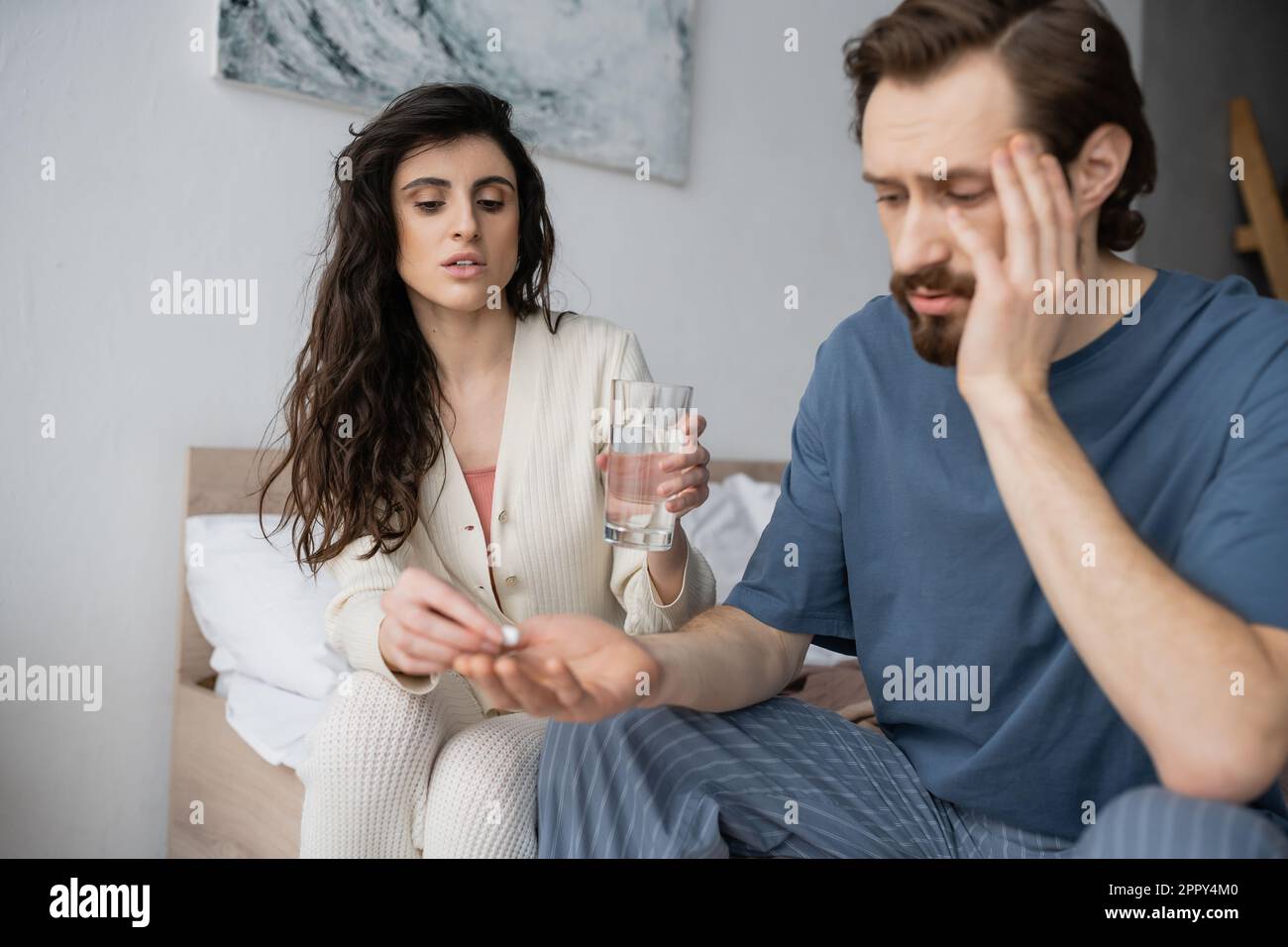 Caring woman giving pill and holding water near blurred boyfriend in bedroom at home,stock image Stock Photo