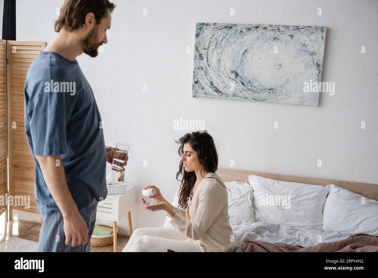 Caring man holding glass of water near girlfriend with pills in bedroom,stock image Stock Photo