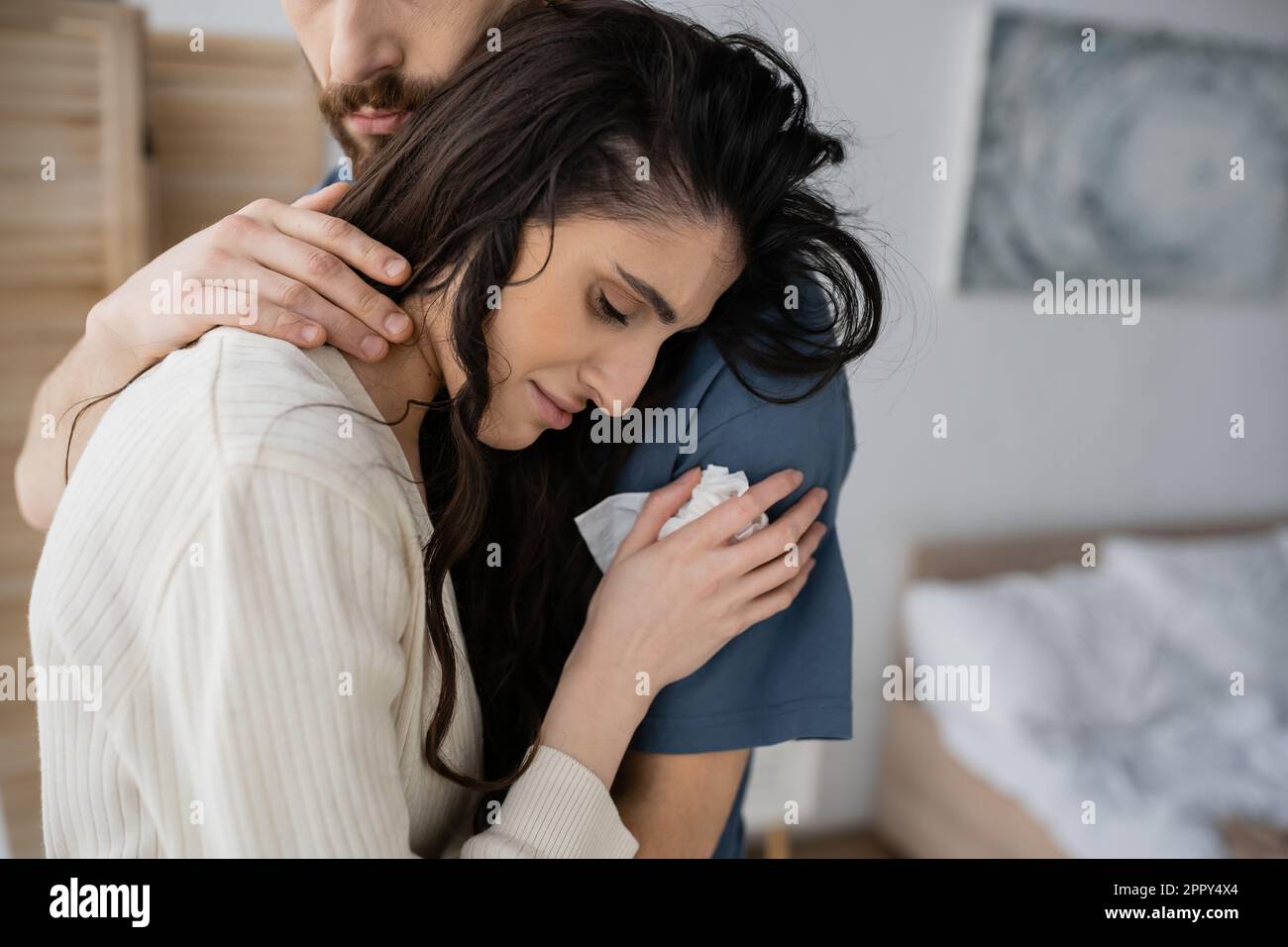 Bearded man calming sad girlfriend with napkin in blurred bedroom,stock image Stock Photo
