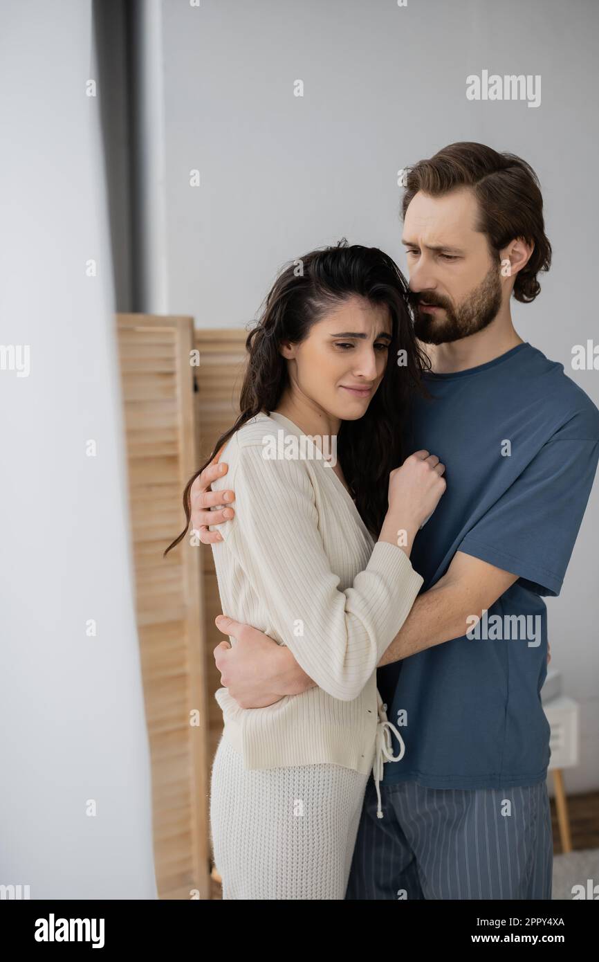 Bearded man in pajama hugging dissatisfied girlfriend at home,stock image Stock Photo
