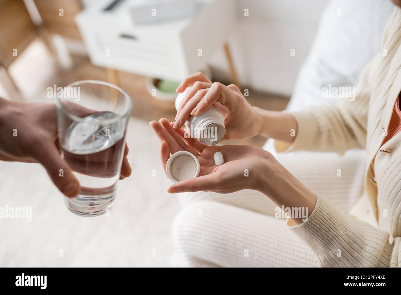 Cropped view of woman pouring pill on hand near boyfriend with glass of water at home,stock image Stock Photo