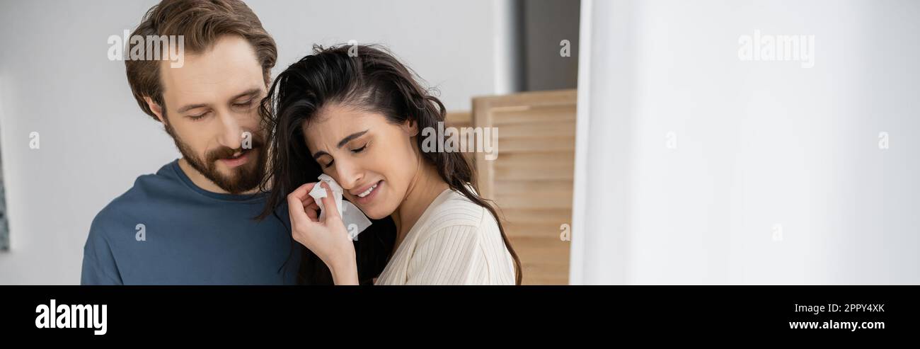 Displeased woman holding napkin and crying near bearded boyfriend at home, banner,stock image Stock Photo