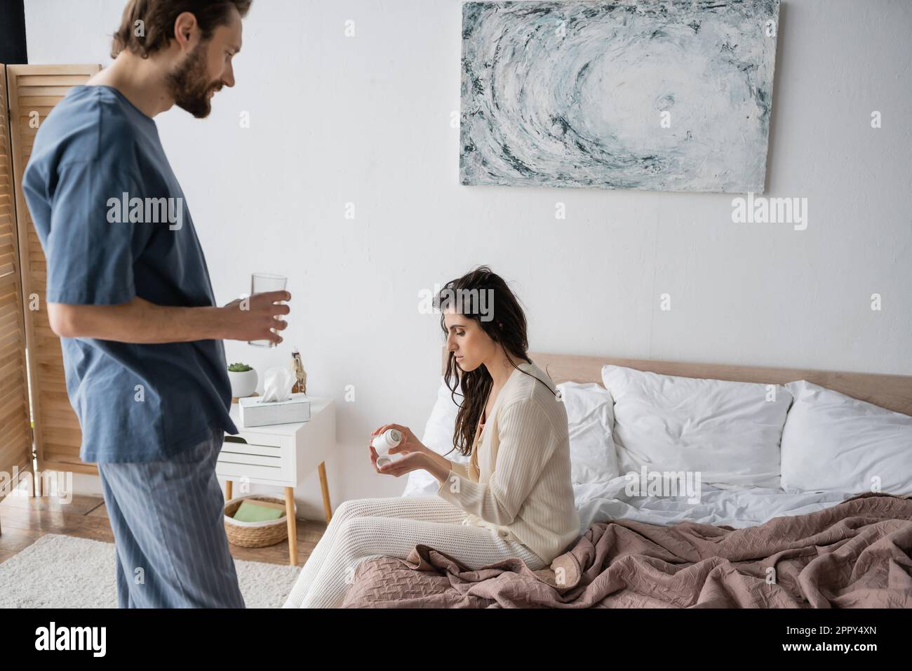 Side view of woman holding pills near caring boyfriend with glass of water in bedroom,stock image Stock Photo