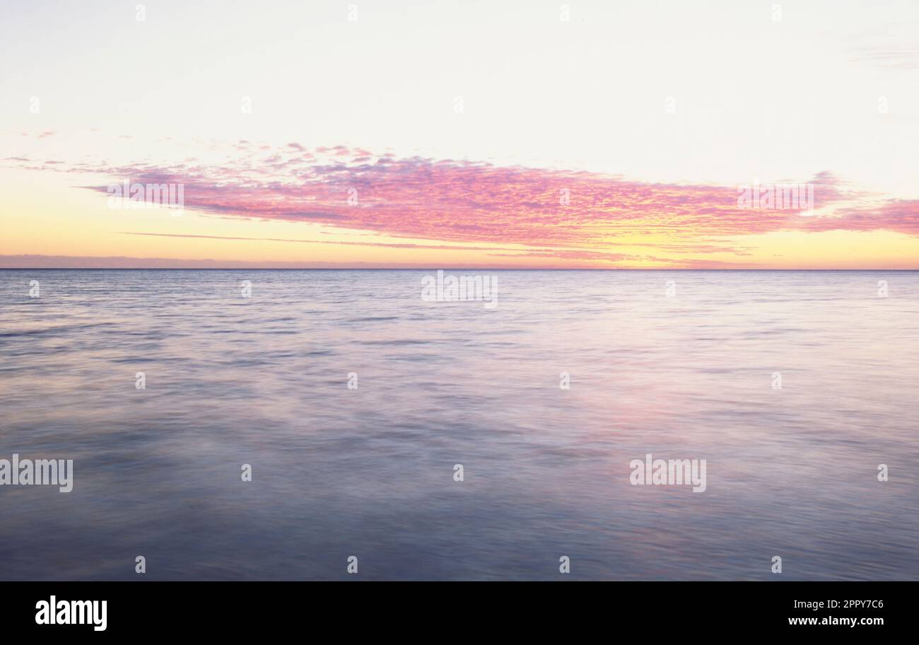 Sun setting behind clouds and over calm tropical ocean Stock Photo