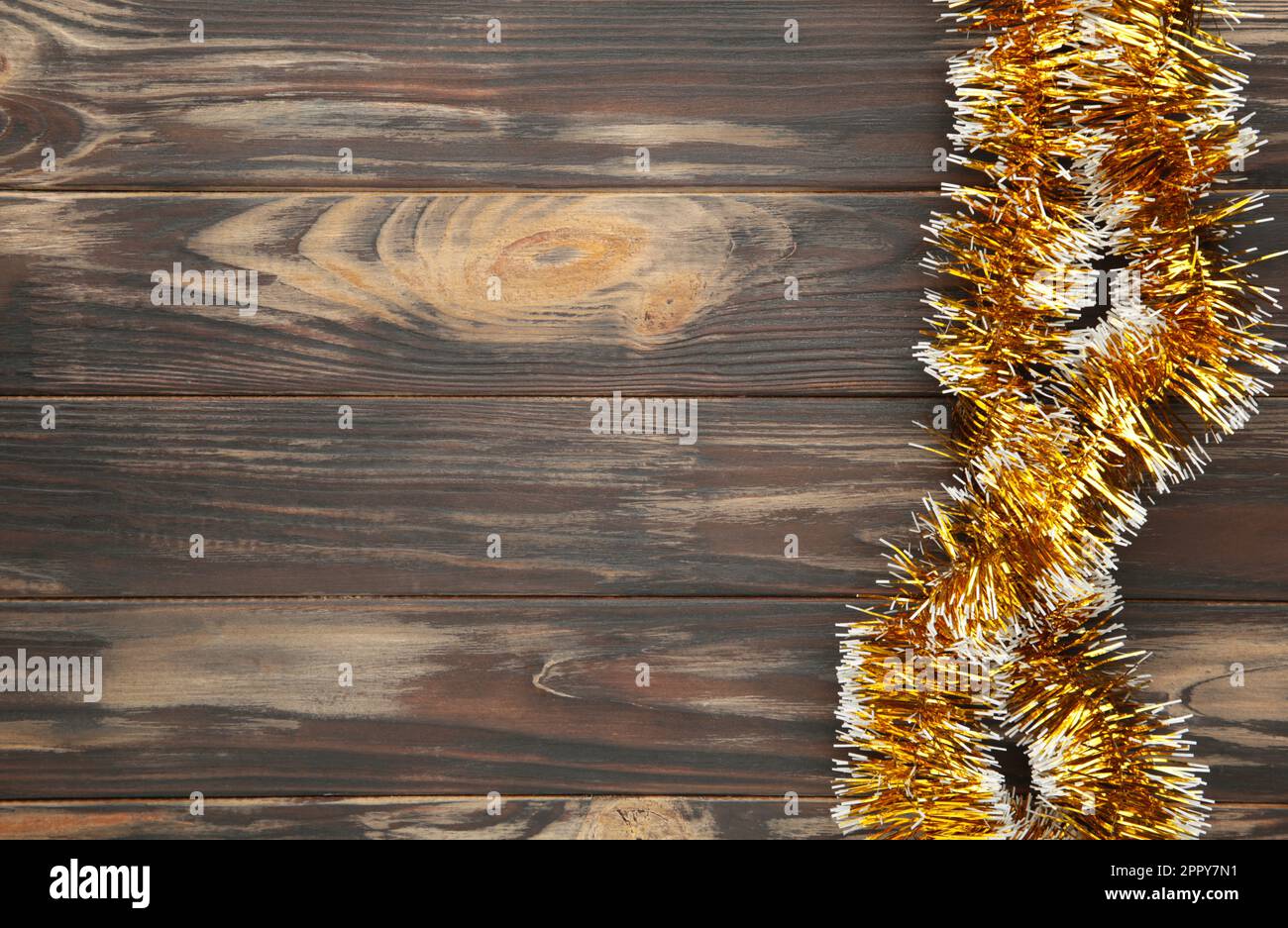 Christmas gold tinsel on brown wooden background. Top view. Stock Photo
