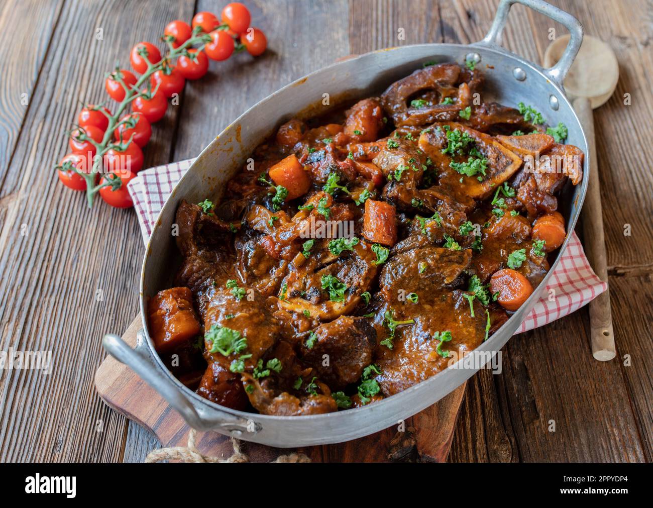 Braised beef shanks or ossubuco with gravy and root vegetables in a old fashioned roasting pan isolated on wooden table from above Stock Photo