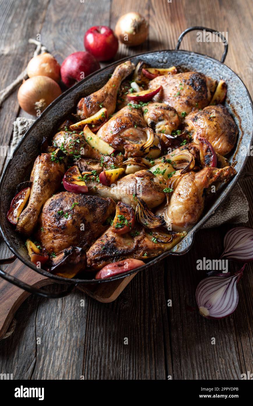 Braised chicken with onions and apples in a old fashioned roasting pan isolated on wooden table Stock Photo