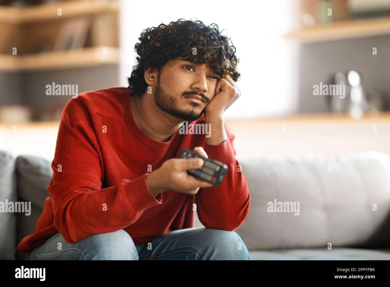 Portrait Of Bored Upset Young Indian Guy Watching TV At Home Stock Photo