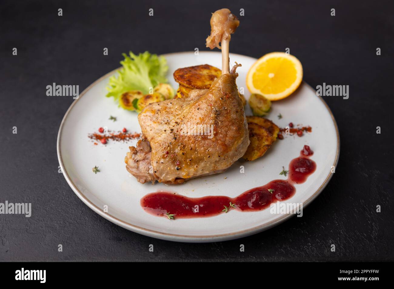 Duck leg confit with Brussels sprouts, baked potatoes, thyme, orange and lingonberry sauce. Traditional French cuisine. Selective focus, close-up, bla Stock Photo
