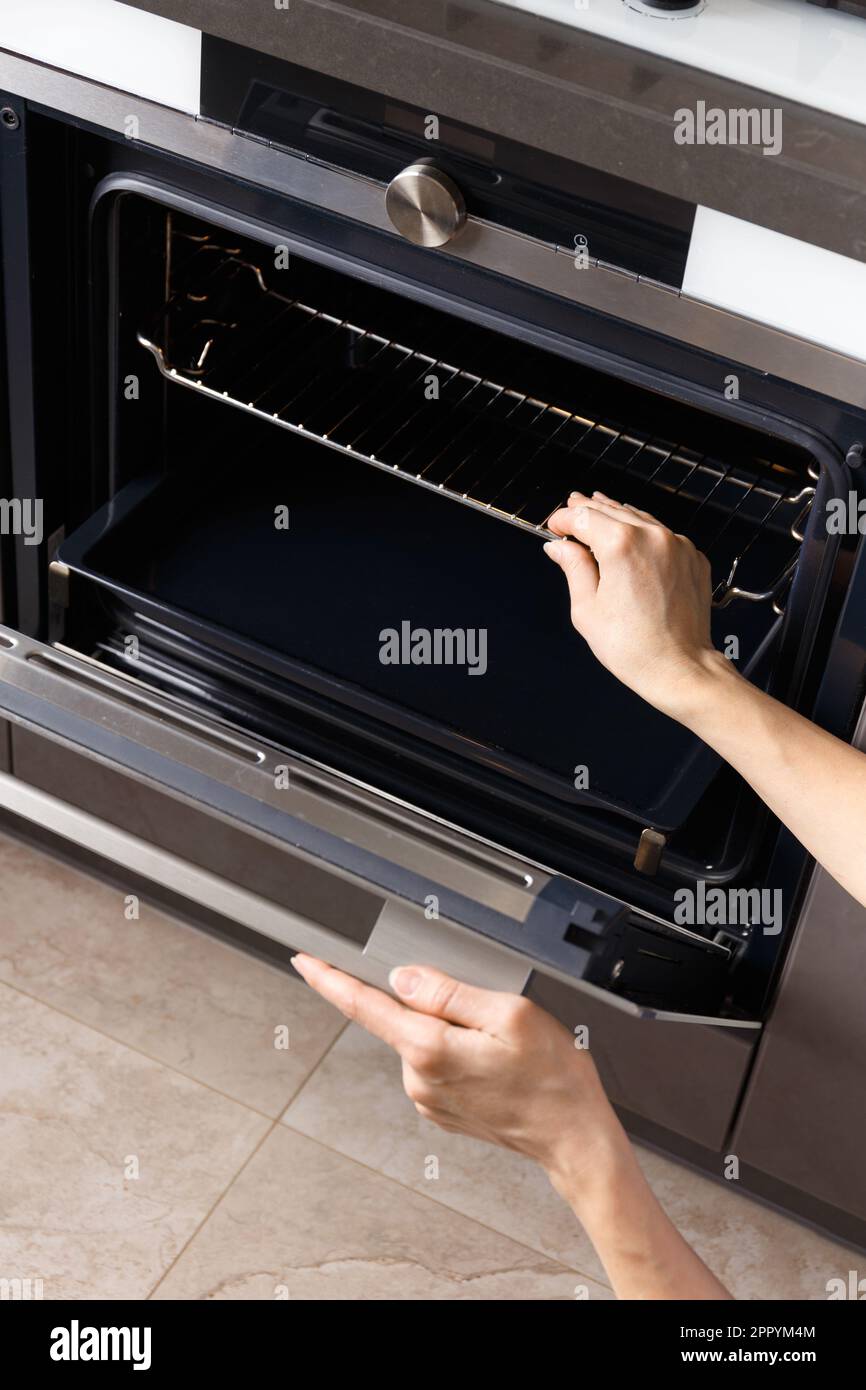 The girl opens the builtin oven door and takes out a baking sheet