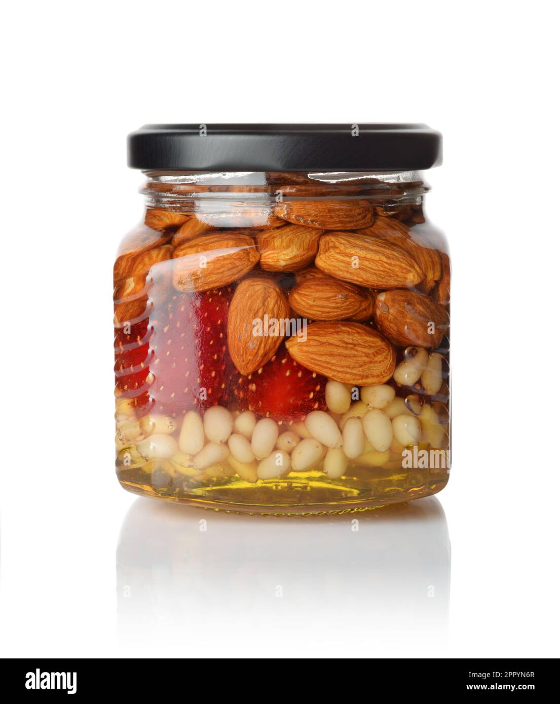 A honey jar with pine nuts and a spoon for honey on white backgr