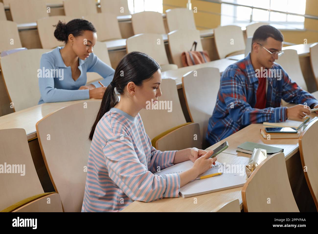 Group of students sitting at desk with books using mobile phones during ...