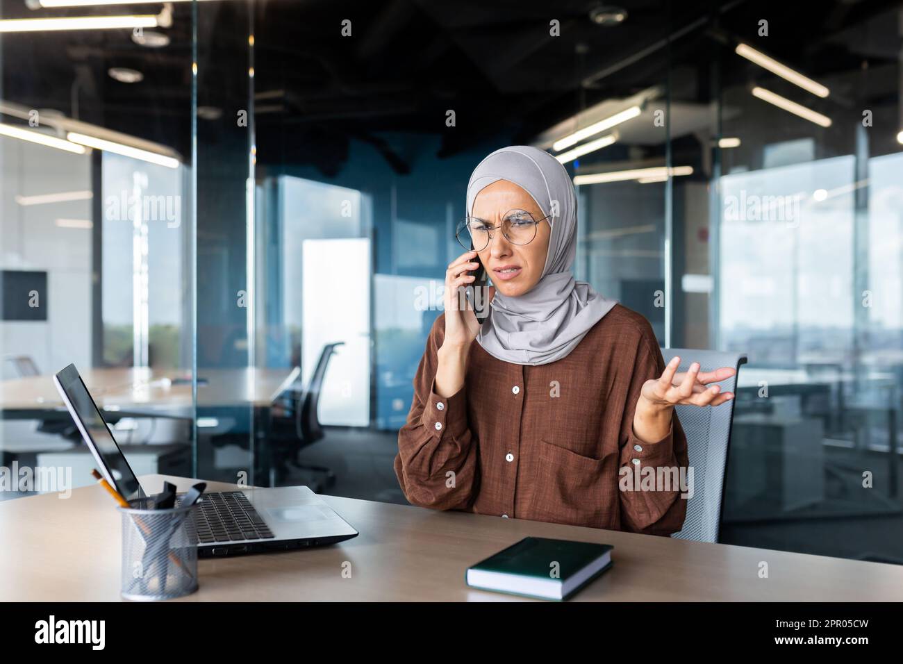 Worried young muslim woman in hijab sitting in office and talking on ...