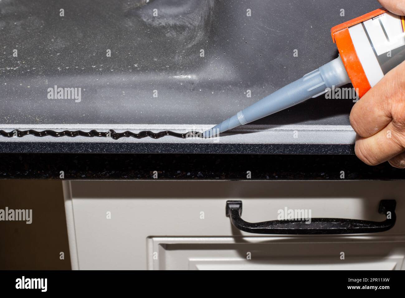 A man applies adhesive sealant to the rim of a countertop kitchen sink. Sink installation Stock