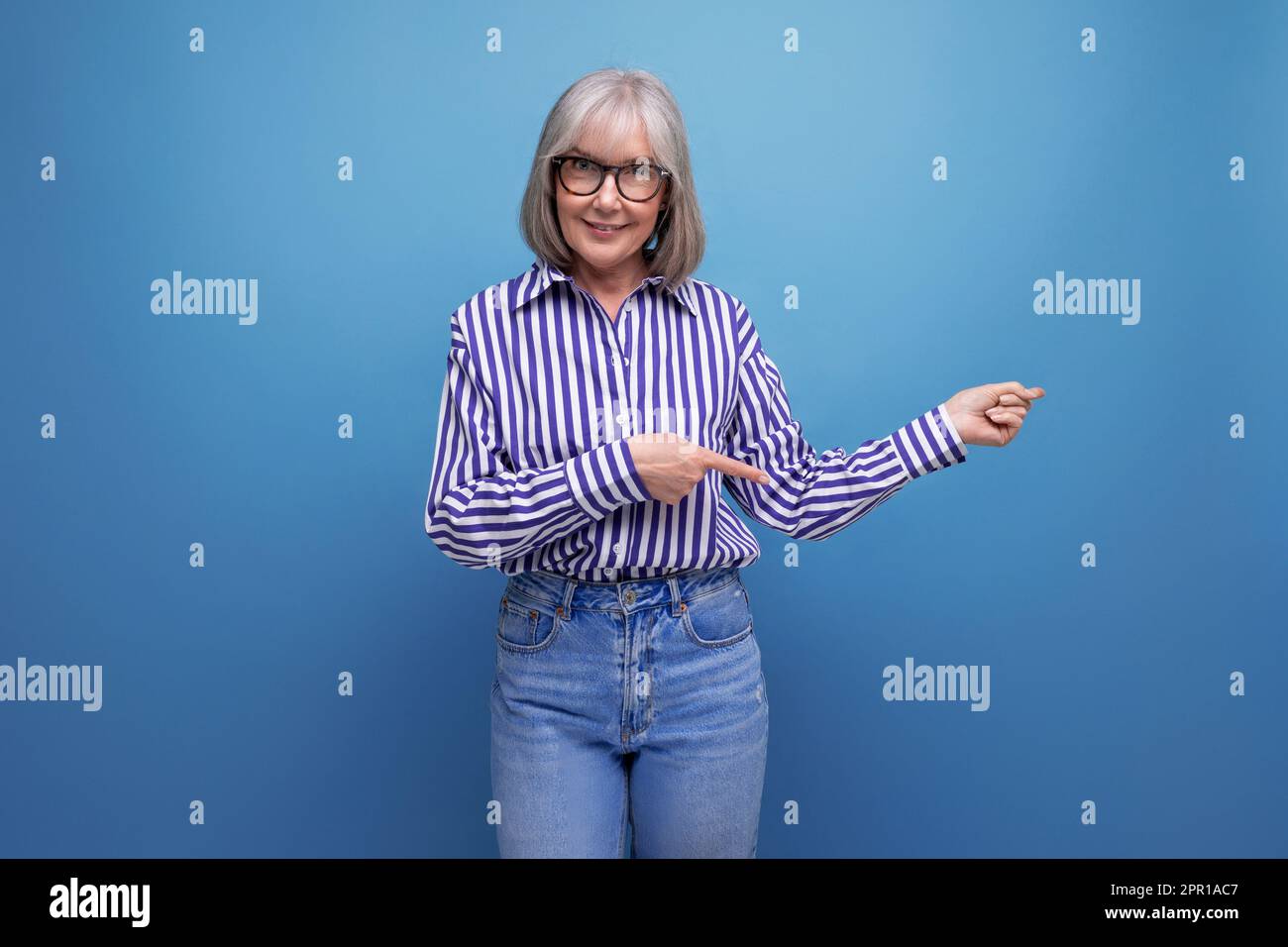 modern 60s middle aged woman with gray hair in a stylish look shows her hand at a banner on a bright studio background with copy space Stock Photo