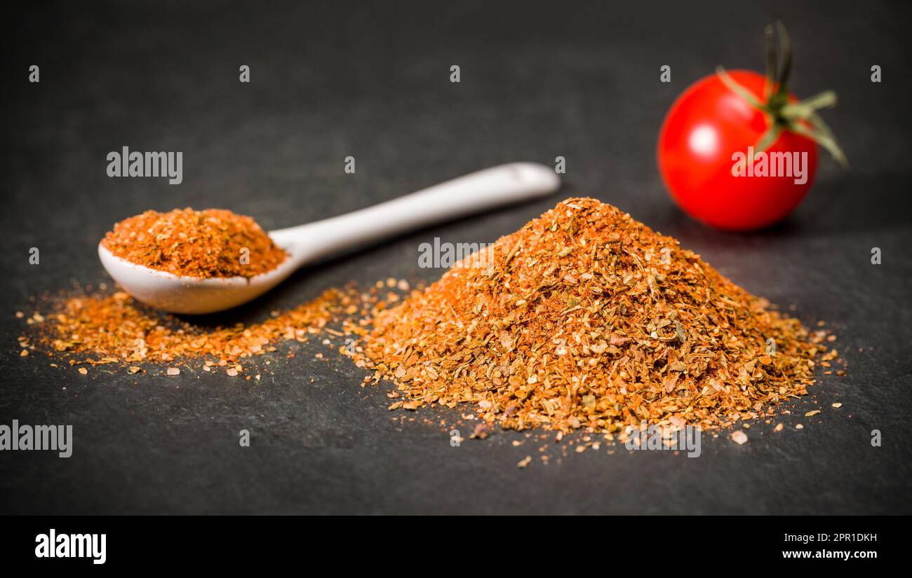 Spices on a spoon and a bunch of dried sun-dried tomatoes next to cherry tomato on the table. Stock Photo