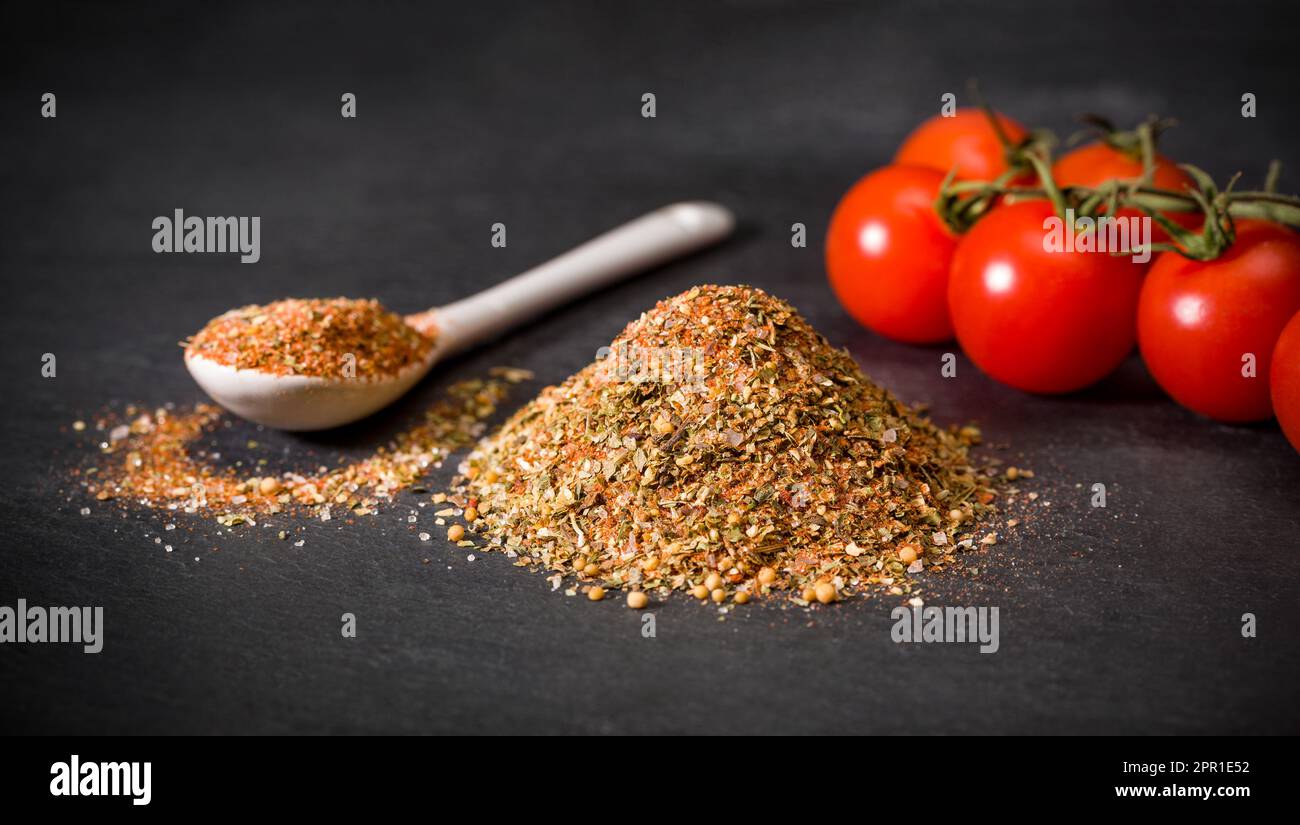 Spices on a spoon and a bunch of dried sun-dried tomatoes next to cherry tomatoes on a branch. Stock Photo