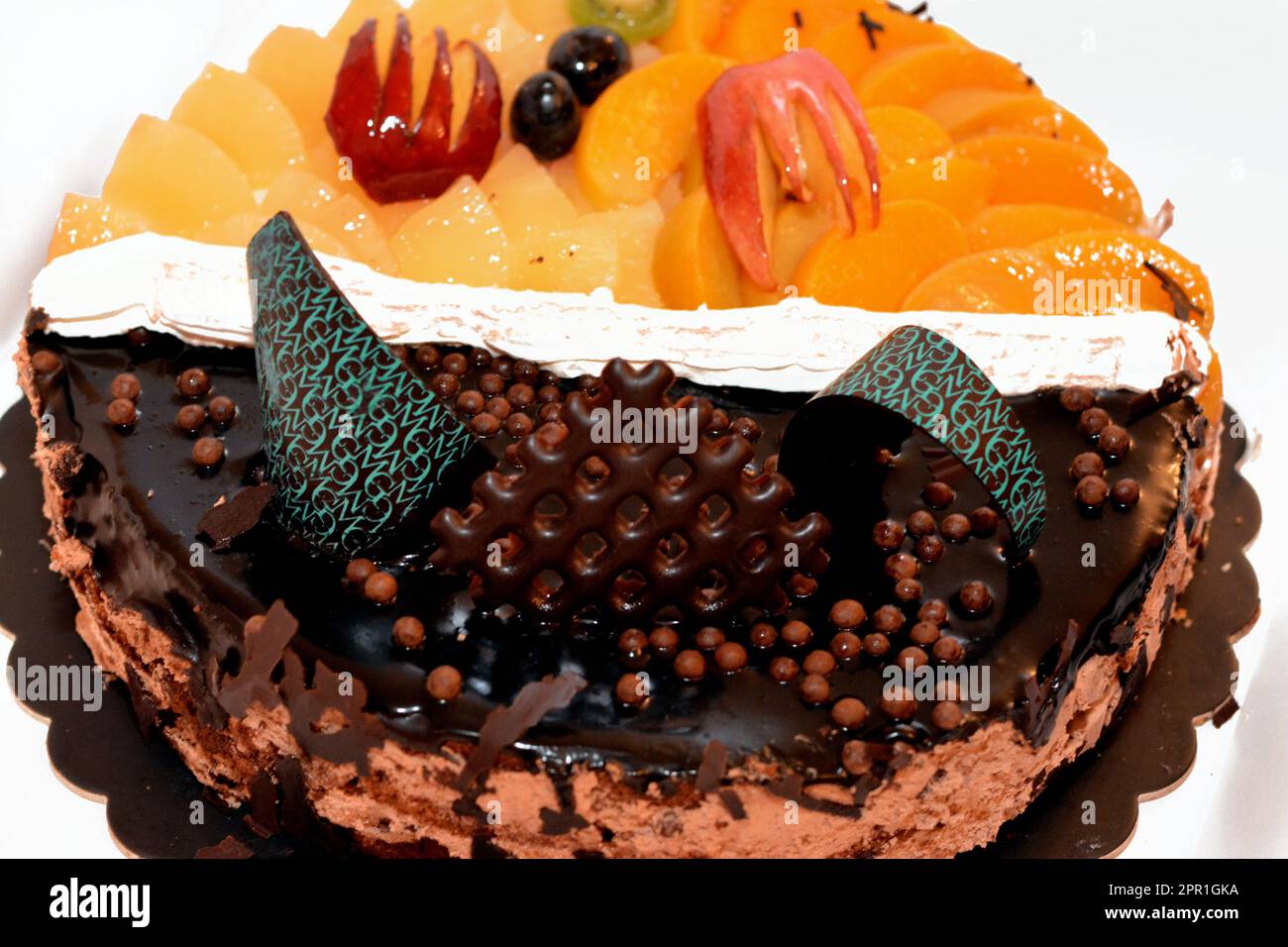 Fresh birthday cake with chocolate bars and pieces, whipped cream, slices of pineapples, apples, black grapes, peach and cherry, a top view of a baked Stock Photo