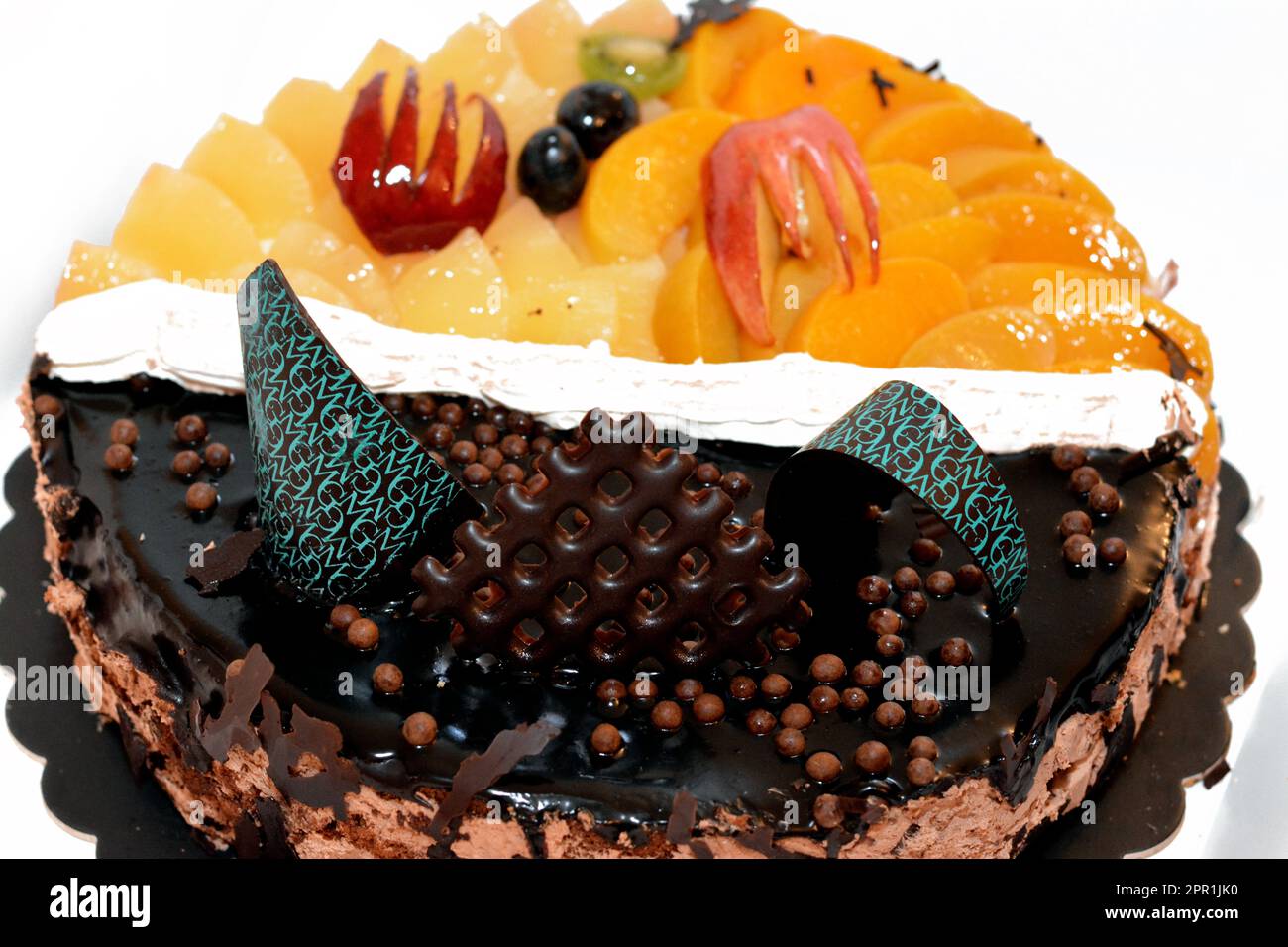 Fresh birthday cake with chocolate bars and pieces, whipped cream, slices of pineapples, apples, black grapes, peach and cherry, a top view of a baked Stock Photo