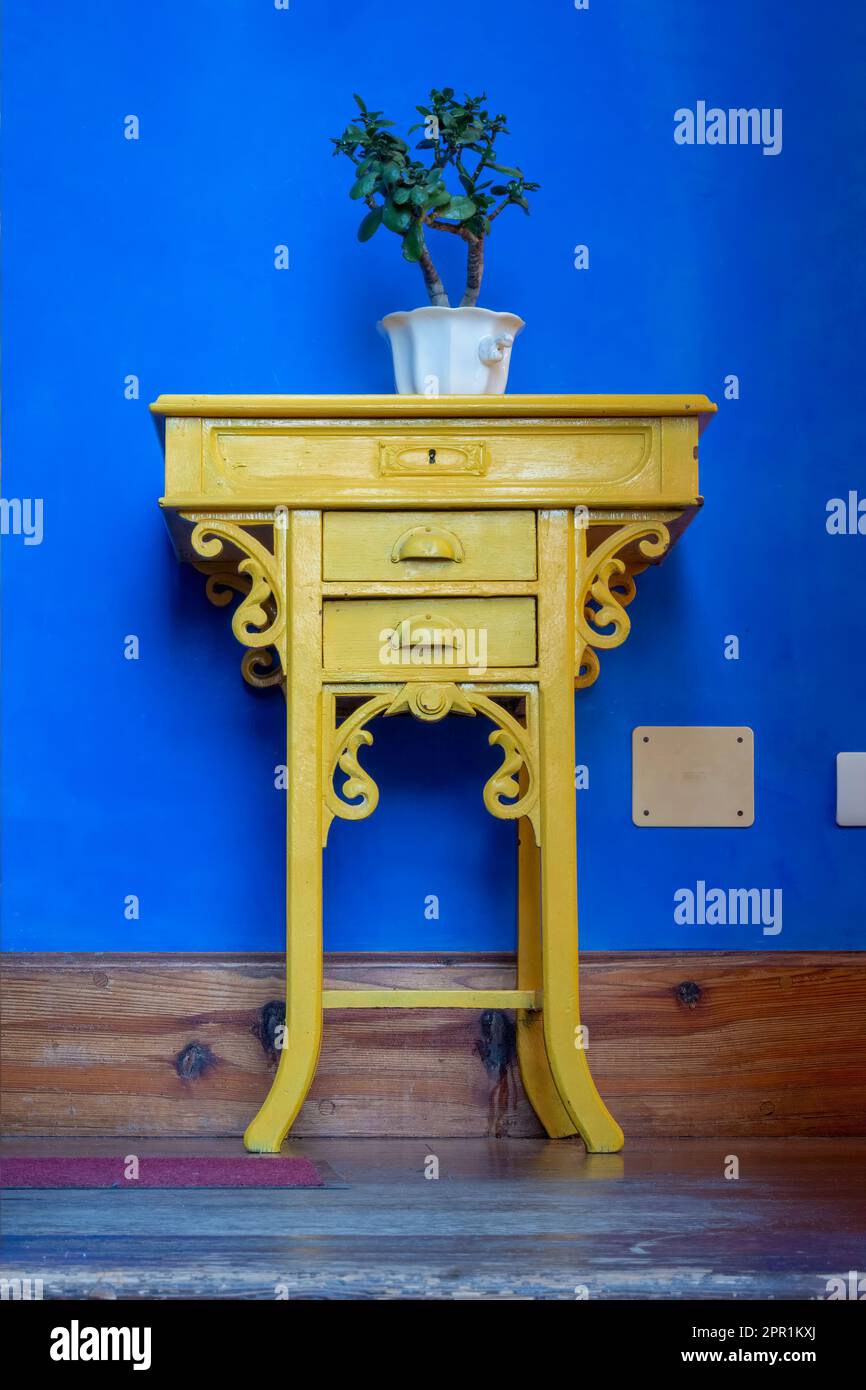 Home decor. Old piece of furniture painted yellow with a flowerpot on top and a blue wall in the background Stock Photo