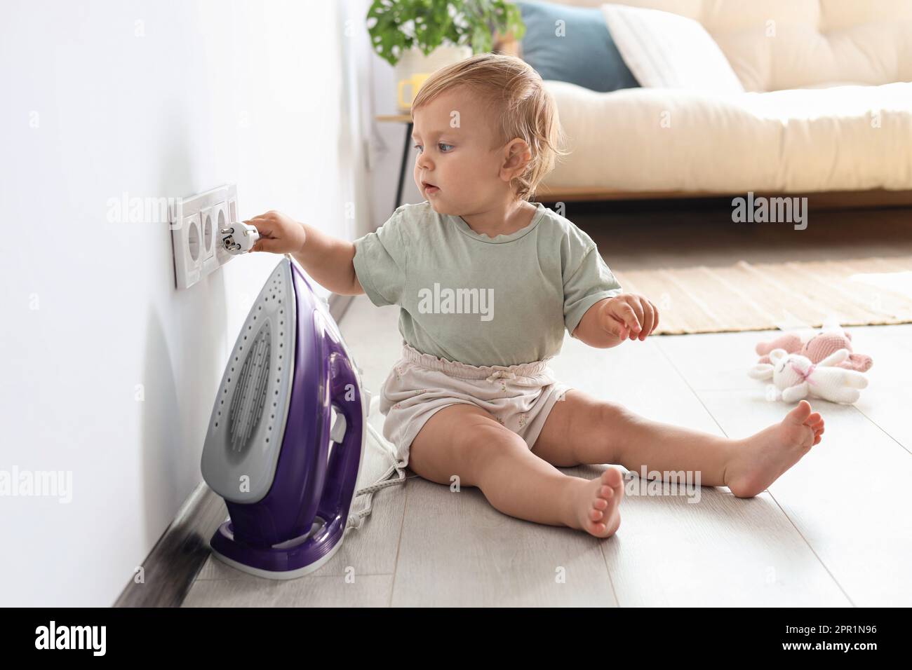 Cute baby playing with electrical socket and iron plug at home